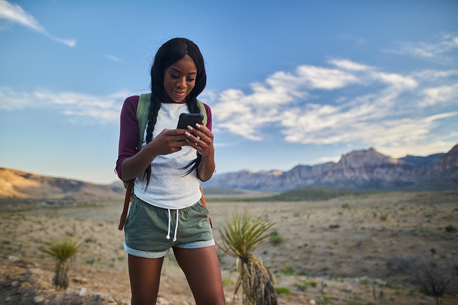 Contact Us - Young Woman Makes a Call While Hiking in the Southwest, Hair in Pigtails, Wearing Shorts and a Backpack