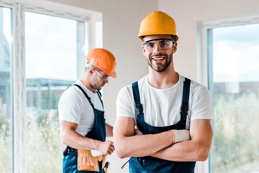 Specialized Business Insurance - Two Construction Workers Stand in an Unfinished Home, Wearing Blue Overalls and Orange Hardhats